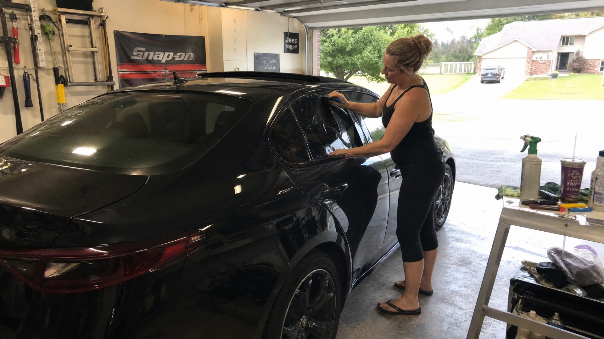 Jenn wiping down the tinted rear door of a black Alfa Romeo Giulia in her garage.