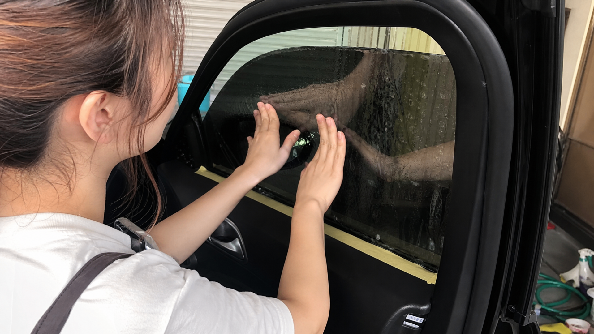 Sarah pressing both hands against freshly applied dark tint on a rear door window.
