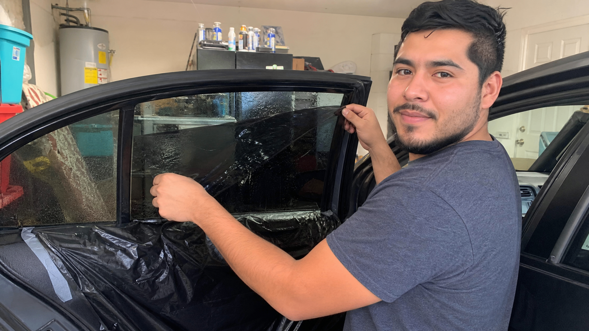 Diego smiling as he peels the liner off precut tint on the rear door of a Volkswagen Jetta.