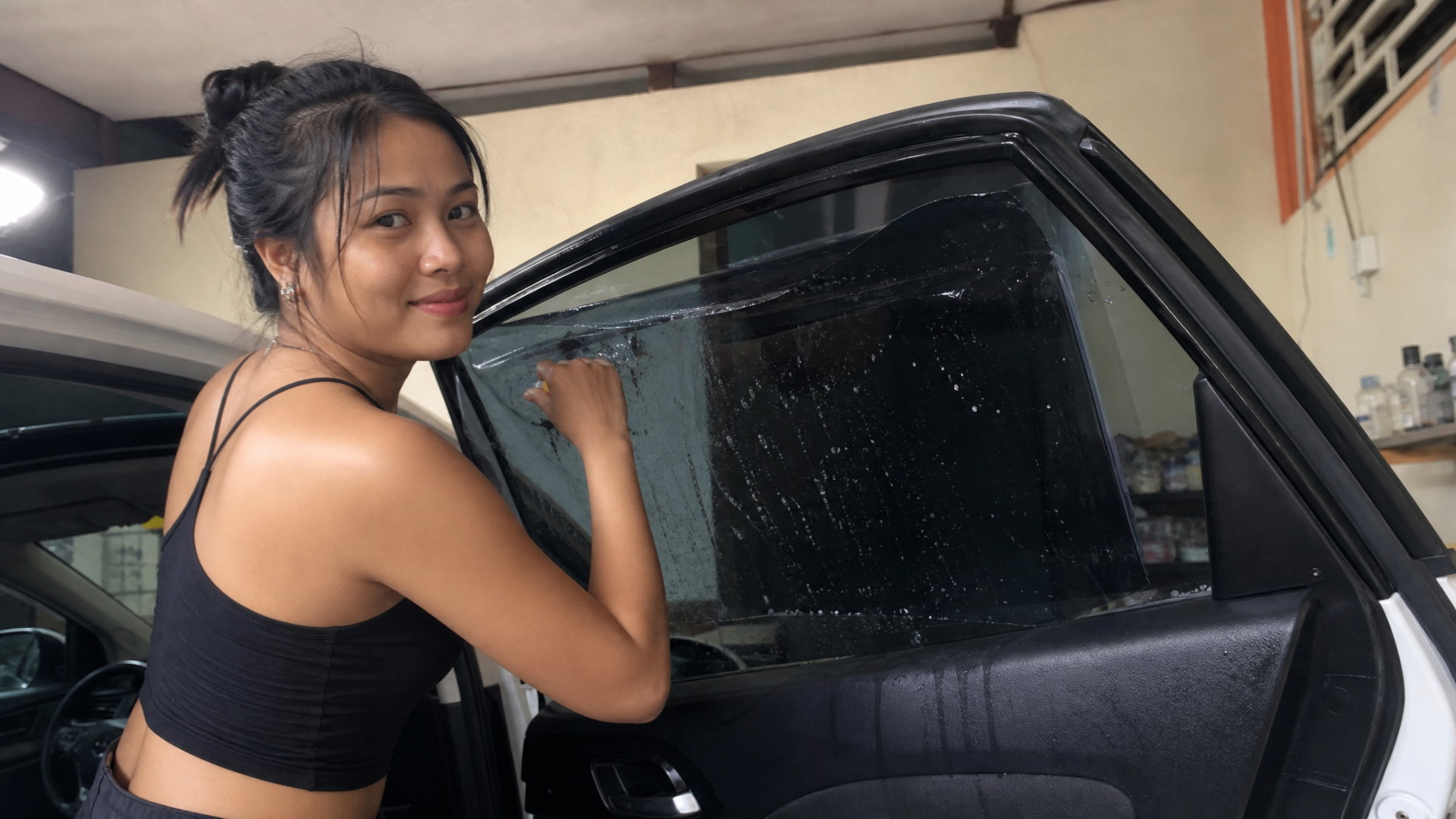 Kayla smiling while installing dark window tint on a white SUV door window.